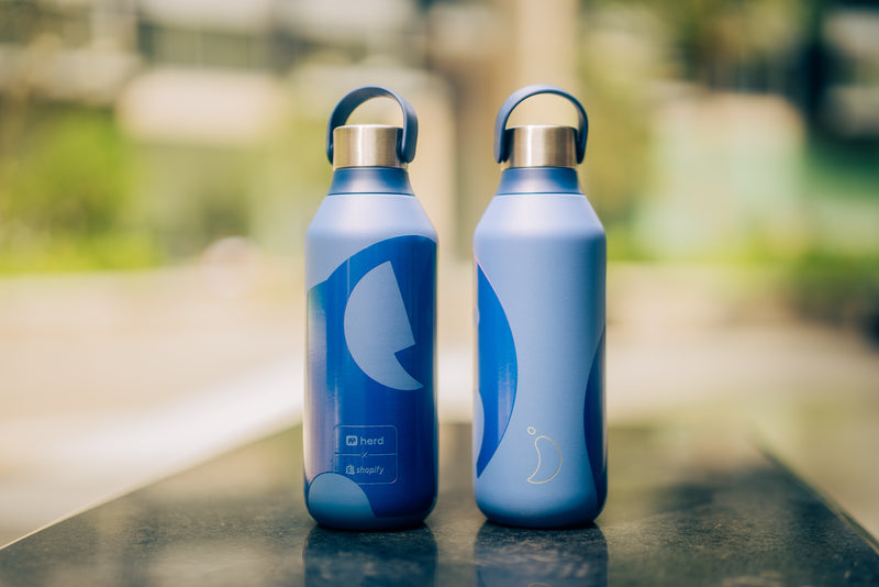 Two blue Herd Chilly's water bottles with Herd brand logo in outdoor setting